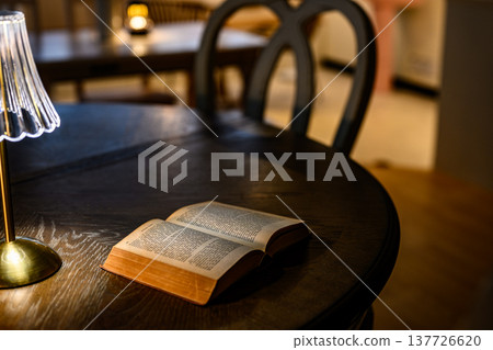 桌上放著一本打開的古董書和一盞燈。 137726620