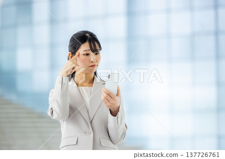 一位年輕的女商人一邊看著她的智慧型手機，一邊心事重重。 137726761