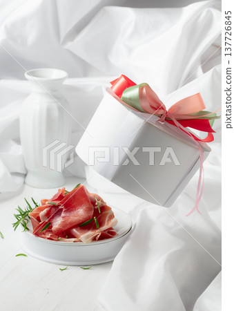Prosciutto with rosemary in gift box on a white wooden table. Prosciutto with rosemary in gift box on a white wooden table. 137726845