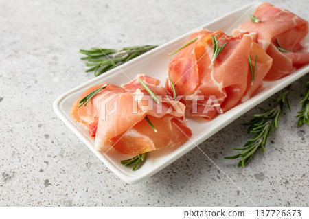 Prosciutto slices with rosemary on a stone table. 137726873