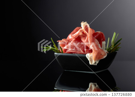 Prosciutto with rosemary on a black background. 137726880