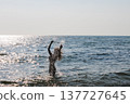Young woman in the sparkling summer sea shining silhouette with water splashes 137727645