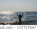 Young woman playing with water splashes while going into the sea to swim on a sunny day 137727647