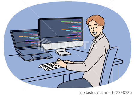 Man programmer types code and looks at camera, sitting at table with computer and laptop 137728726
