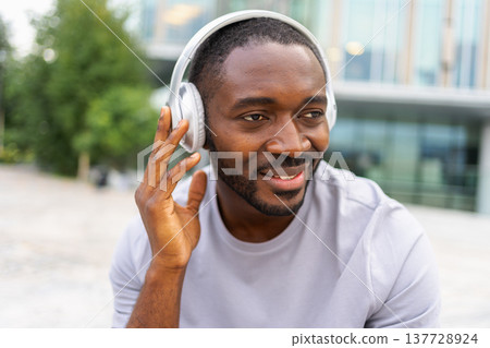 Music song concept. Good start day. Happy African American man listening modern hit on street in city. Person guy wearing headphones enjoy listening favorite music outdoor. People lifestyle joy 137728924