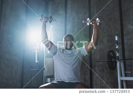 Fitness workout in gym. African American man bodybuilder picking up dumbbells in gym. Workout weight training biceps muscles with dumbbell in fitness club. Man doing sports exercise. Healthy lifestyle Fitness workout in gym. African American man bodybuilder picking up dumbbells in gym. Workout weight training biceps muscles with dumbbell in fitness club. Man doing sports exercise. Healthy lifestyle 137728953