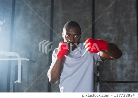 Workout in gym. African man fighter ready for fight punching with boxing wraps protective bandages to camera. Strong man training punches looking concentrated straight preparing for boxing sparring 137728954
