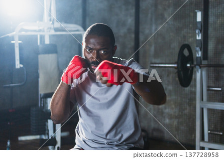Fitness workout in gym. African man fighter preparing for fight punching with red boxing wraps sports protective bandages in gym. Strong man training punches ready for fight boxing sparring training 137728958