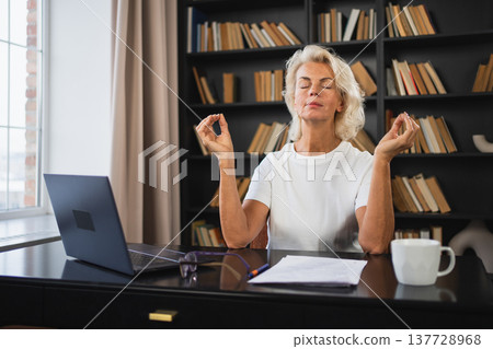 Yoga mindfulness meditation No stress keep calm. Middle aged woman practicing yoga at office. Woman taking break from work meditating relaxing. Mature lady doing breathing practice online yoga at work 137728968