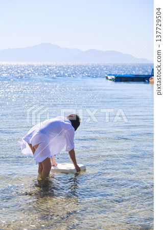A woman places a chair in the sea for a photo shoot A woman places a chair in the sea for a photo shoot 137729504