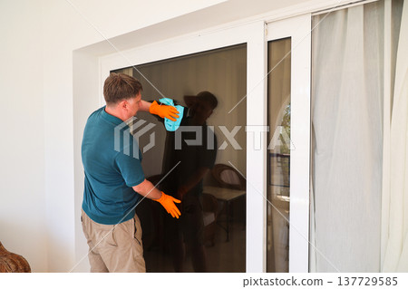 A man wipes dust from a large picture window in his home A man wipes dust from a large picture window in his home 137729585