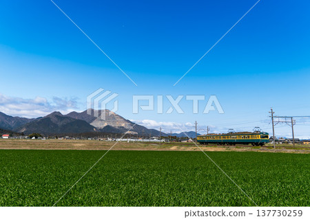 A green train on the Sangi Railway Sangi Line runs through a clear blue sky with Mount Fujiwara in the background. A green train on the Sangi Railway Sangi Line runs through a clear blue sky with Mount Fujiwara in the background. 137730259