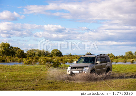 Japanese SUV moving by a puddle making a lot of water splashes Japanese SUV moving by a puddle making a lot of water splashes 137730380