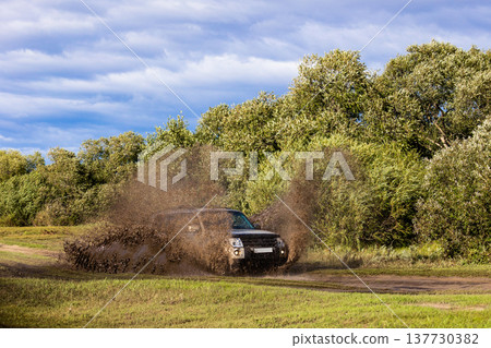 Japanese SUV moving by a puddle making a lot of dirt splashes Japanese SUV moving by a puddle making a lot of dirt splashes 137730382