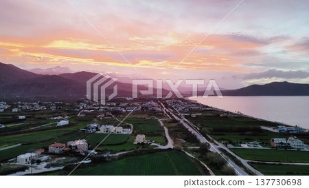Aerial panoramic view of Crete coastline at twilight with colorful pre-sunset sky, valley with fields and villages, mountain ridge, and reflective sea bay Aerial panoramic view of Crete coastline at twilight with colorful pre-sunset sky, valley with fields and villages, mountain ridge, and reflective sea bay 137730698