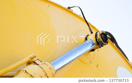 Close up view of hydraulic cylinder and piston rod on heavy construction machinery. Industrial engineering detail, mechanical power system, and equipment durability for infrastructure and maintenance. 137730715