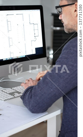 Architect designing building plans on computer, typing at desk with architectural model and blueprints. Business and architecture concept Architect designing building plans on computer, typing at desk with architectural model and blueprints. Business and architecture concept 137731380