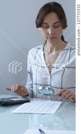 Accountant carefully reviewing financial documents, magnifying details, calculating performance metrics at professional workspace. Audit and taxes in business Accountant carefully reviewing financial documents, magnifying details, calculating performance metrics at professional workspace. Audit and taxes in business 137731410
