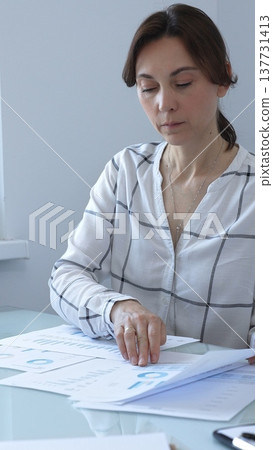 Businesswoman reviewing financial data, analyzing charts and graphs while working on a project at her office desk, demonstrating focus and expertise in business management. Business people concept Businesswoman reviewing financial data, analyzing charts and graphs while working on a project at her office desk, demonstrating focus and expertise in business management. Business people concept 137731413