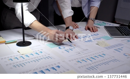 Business professionals analyzing financial data and marketing reports on a white desk, collaborating on project strategy and reviewing company performance with charts and diagrams Business professionals analyzing financial data and marketing reports on a white desk, collaborating on project strategy and reviewing company performance with charts and diagrams 137731446
