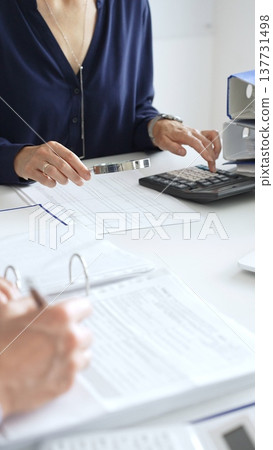 Financial analysts examining documents, using magnifying glass and calculator while studying corporate data at workplace. Audit and taxes in business Financial analysts examining documents, using magnifying glass and calculator while studying corporate data at workplace. Audit and taxes in business 137731498