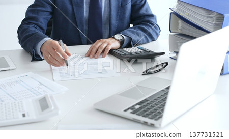 Accountants analyzing financial documents, calculating numbers together at shared workspace with laptop and office supplies surrounding them. Audit and taxes in business Accountants analyzing financial documents, calculating numbers together at shared workspace with laptop and office supplies surrounding them. Audit and taxes in business 137731521