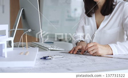 Architect drawing technical plans and working with scale models on a desk with a computer, focusing on design and engineering. Business and architecture concept Architect drawing technical plans and working with scale models on a desk with a computer, focusing on design and engineering. Business and architecture concept 137731522