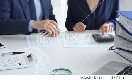 Close up of calculator and magnifying glass over financial documents opposite financial team analyzing data, reviewing reports, collaborating at modern office workspace. Audit and taxes in business Close up of calculator and magnifying glass over financial documents opposite financial team analyzing data, reviewing reports, collaborating at modern office workspace. Audit and taxes in business 137731531