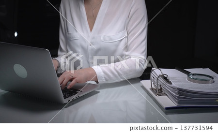 Businesswoman researching documents and accounting data with laptop and magnifying glass working late. Audit and taxes concept Businesswoman researching documents and accounting data with laptop and magnifying glass working late. Audit and taxes concept 137731594