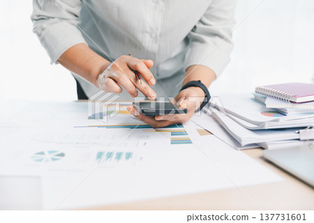 Business professional using calculator and pen reviewing financial report charts on office desk, budgeting and accounting analysis for planning, audit and fintech management workflow. financial report 137731601