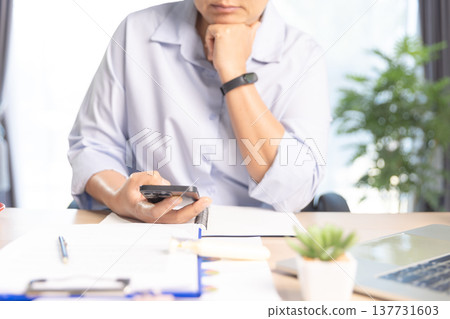 Business professional working on laptop at modern office desk with documents, smartphone and stationery, bright daylight by window. Concept of productivity, remote work and digital management. Business professional working on laptop at modern office desk with documents, smartphone and stationery, bright daylight by window. Concept of productivity, remote work and digital management. 137731603