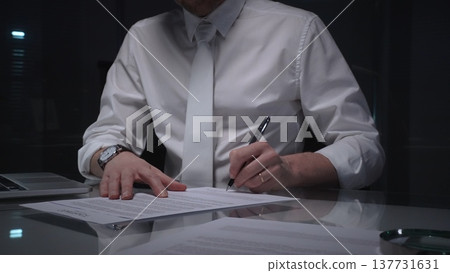 Business man signing a contract late in the office, closing a deal, or completing legal paperwork at deep night. Audit and overworking concepts 137731631