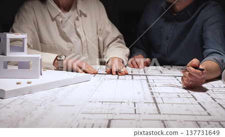 Architects team discussing building blueprint design, collaborating on construction project plans, working on architectural development at night, creating new property layouts 137731649