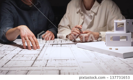 Architects and engineers collaborating on a new building project, planning structural details and design concepts using blueprints and a scaled architectural model on a desktop Architects and engineers collaborating on a new building project, planning structural details and design concepts using blueprints and a scaled architectural model on a desktop 137731653