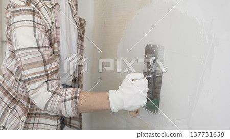 Unknown female construction worker wearing protective gloves applying plaster, smoothing wall surface during home renovation work Unknown female construction worker wearing protective gloves applying plaster, smoothing wall surface during home renovation work 137731659