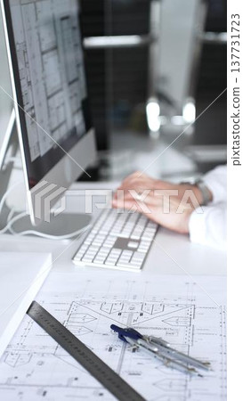 Architect working at desktop computer, checking blueprints and design plans for a new engineering project. Business and architecture concept Architect working at desktop computer, checking blueprints and design plans for a new engineering project. Business and architecture concept 137731723