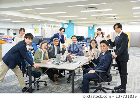 A large group of business people, both male and female, gathered in a spacious office. A large group of business people, both male and female, gathered in a spacious office. 137731839