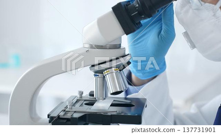 Microscope and scientist's hands in blue gloves adjusting close up in laboratory set. Medicine, science concept 137731901