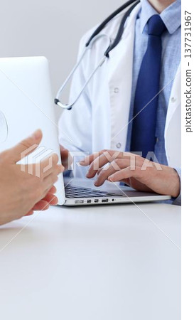 Doctor man is taking notes with laptop while listening to a female patient explaining her symptoms during a medical consultation in the clinic office. Medicine concept Doctor man is taking notes with laptop while listening to a female patient explaining her symptoms during a medical consultation in the clinic office. Medicine concept 137731967