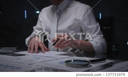 Business professional analyzing financial data with charts and reports on desk, working late in dark office. Audit and overworking concepts Business professional analyzing financial data with charts and reports on desk, working late in dark office. Audit and overworking concepts 137731979