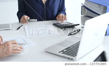 Business team of business man and female entrepreneur analyzing financial documents, using calculators and laptop, working together on project in modern office. Audit and taxes concept Business team of business man and female entrepreneur analyzing financial documents, using calculators and laptop, working together on project in modern office. Audit and taxes concept 137731995