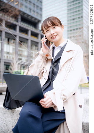 A young businesswoman checks her laptop while on a call while out and about. A young businesswoman checks her laptop while on a call while out and about. 137732691