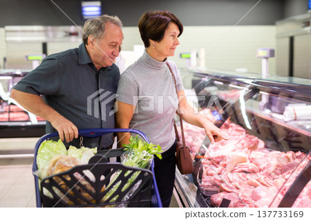 Mature couple choosing piece of meat in meat department in grocery store Mature couple choosing piece of meat in meat department in grocery store 137733169