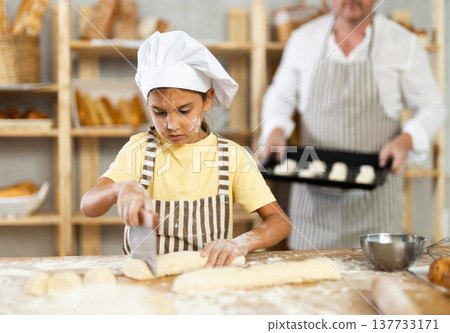 Little girl, baker assistant, cutting raw dough with knife Little girl, baker assistant, cutting raw dough with knife 137733171