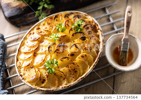Golden-brown gratin potatoes, neatly arranged in a white ceramic bowl and garnished with fresh herbs. In Slovakia, however, this dish is known primarily at home as French potatoes 137734564