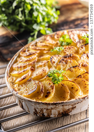 Golden-brown gratin potatoes, neatly arranged in a white ceramic bowl and garnished with fresh herbs. In Slovakia, however, this dish is known primarily at home as French potatoes 137734569