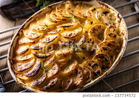 Golden-brown gratin potatoes, neatly arranged in a white ceramic bowl and garnished with fresh herbs. In Slovakia, however, this dish is known primarily at home as French potatoes 137734572