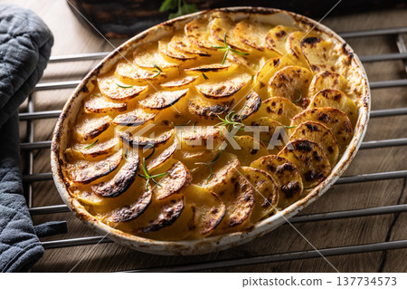 Golden-brown gratin potatoes, neatly arranged in a white ceramic bowl and garnished with fresh herbs. In Slovakia, however, this dish is known primarily at home as French potatoes 137734573