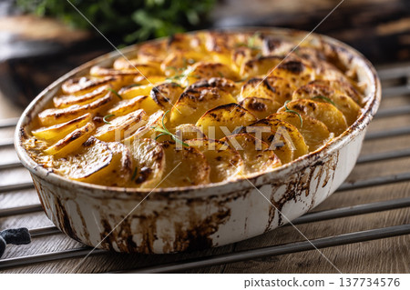 Golden-brown gratin potatoes, neatly arranged in a white ceramic bowl and garnished with fresh herbs. In Slovakia, however, this dish is known primarily at home as French potatoes 137734576
