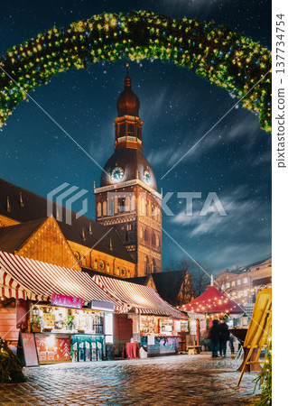 Riga, Latvia. Traditional Christmas Market On Dome Square With Cathedral. Famous Landmark In Winter Evening Night In Festive Illuminations Lighting Riga, Latvia. Traditional Christmas Market On Dome Square With Cathedral. Famous Landmark In Winter Evening Night In Festive Illuminations Lighting 137734754